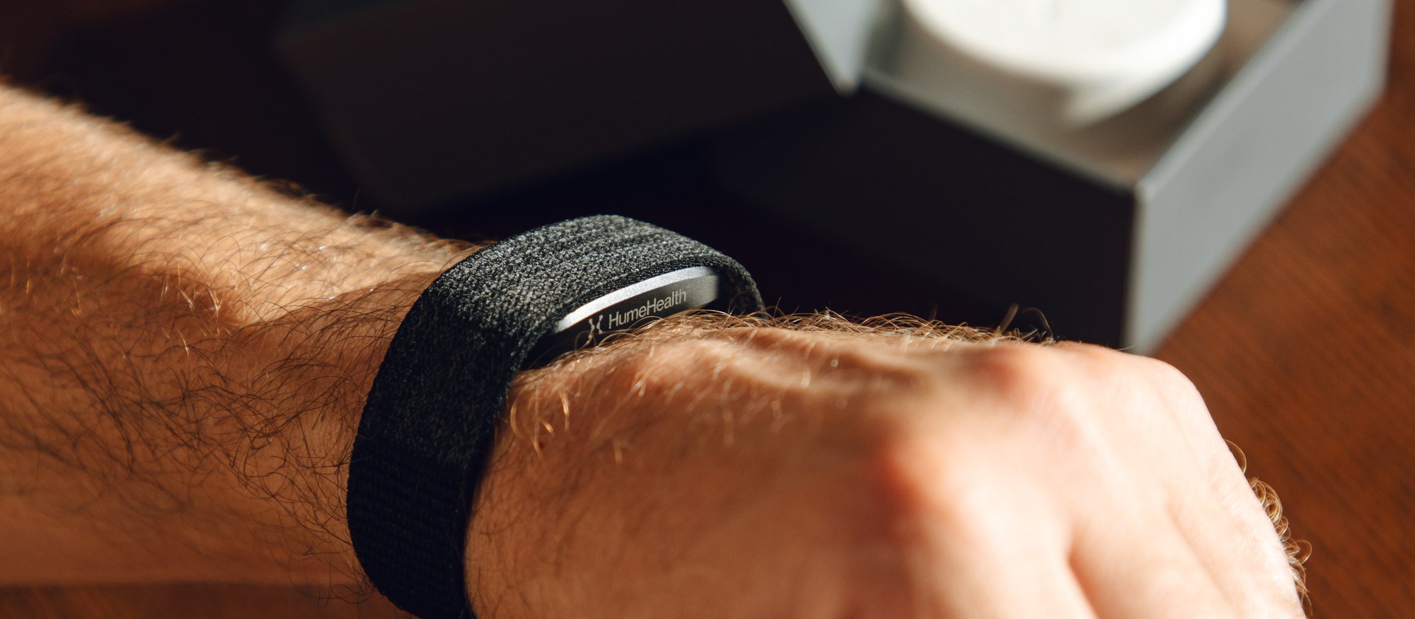 A person fastening the Hume Band 2.0 on their wrist beside its packaging